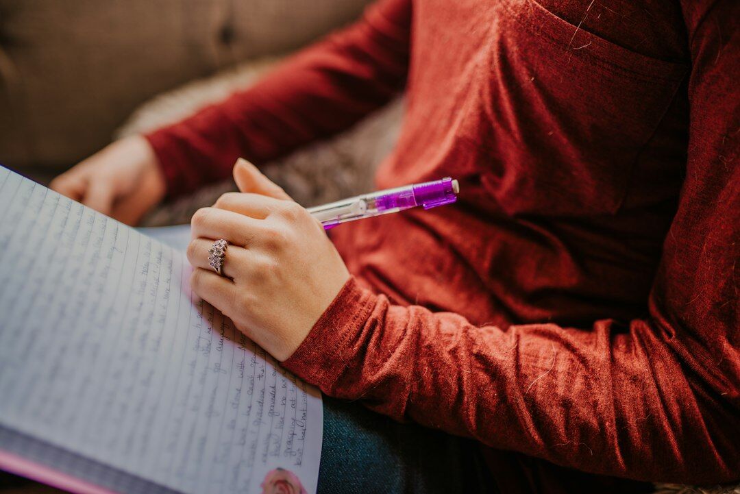 Hands writing reflections in an open notebook on a wooden desk